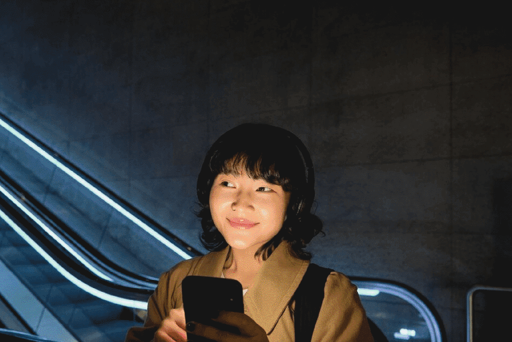 Person using smartphone with escalator and blue lights in the background.