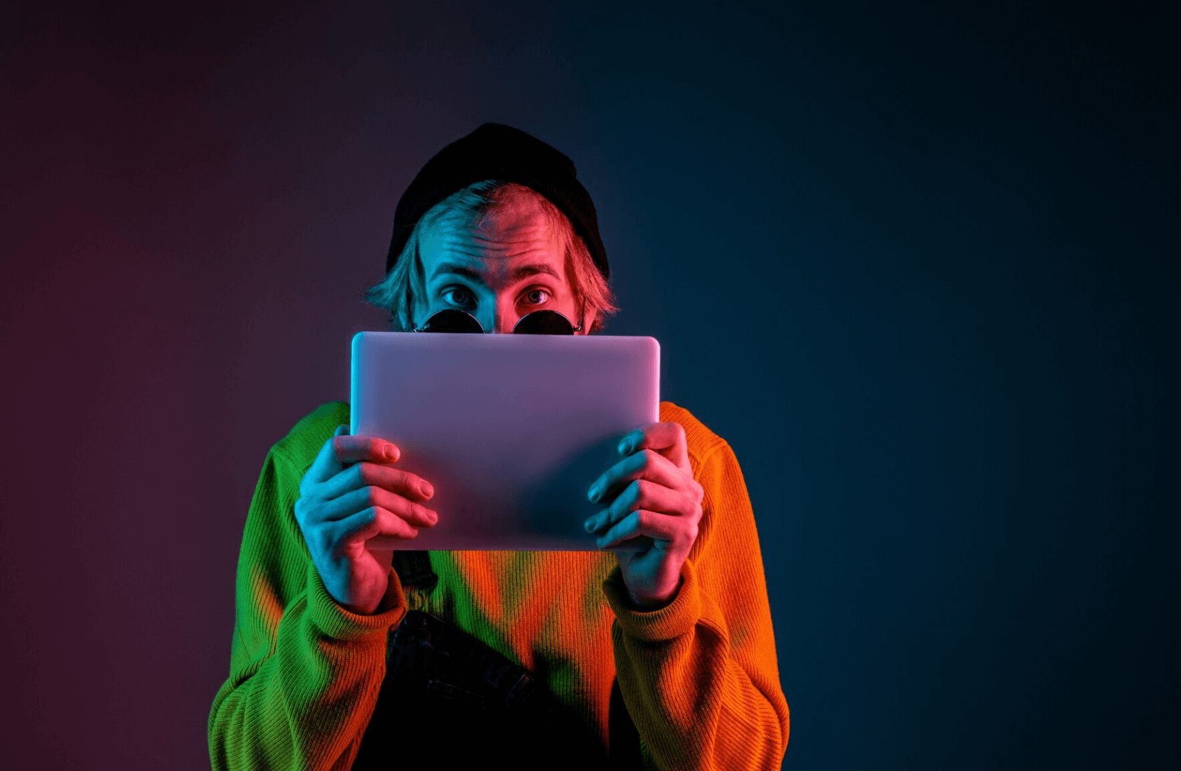 Person in a beanie and sweater holding a tablet with colorful neon lighting.